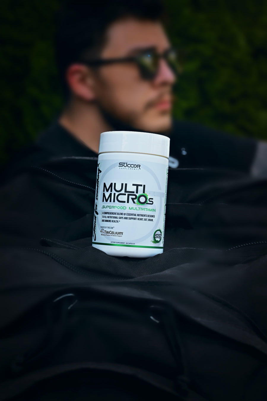 Person wearing sunglasses with a supplement container labeled 'Multi Micros' in the foreground
